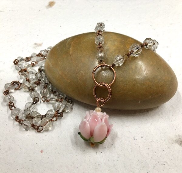 Necklace of a delicate pink lampwork glass flower bead with green leaves on copper jump rings with clear glass beaded rosary chain. 